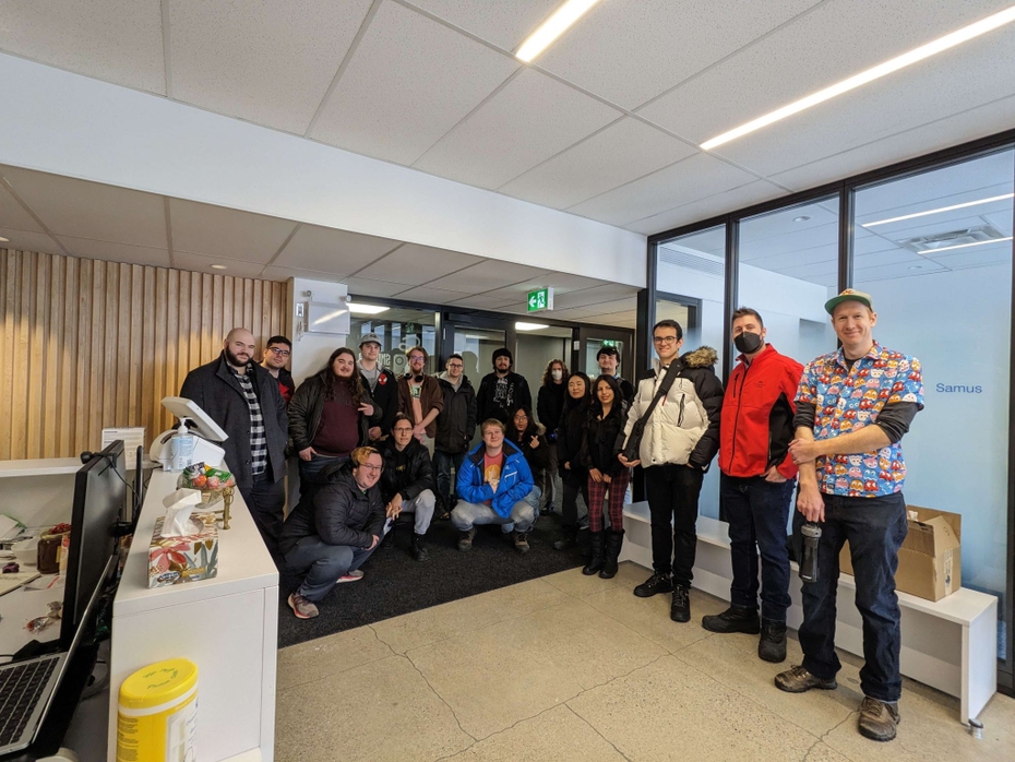 Students and faculty from the college's Game Programming program stand as a group in the lobby of Snowed In Studios Inc.